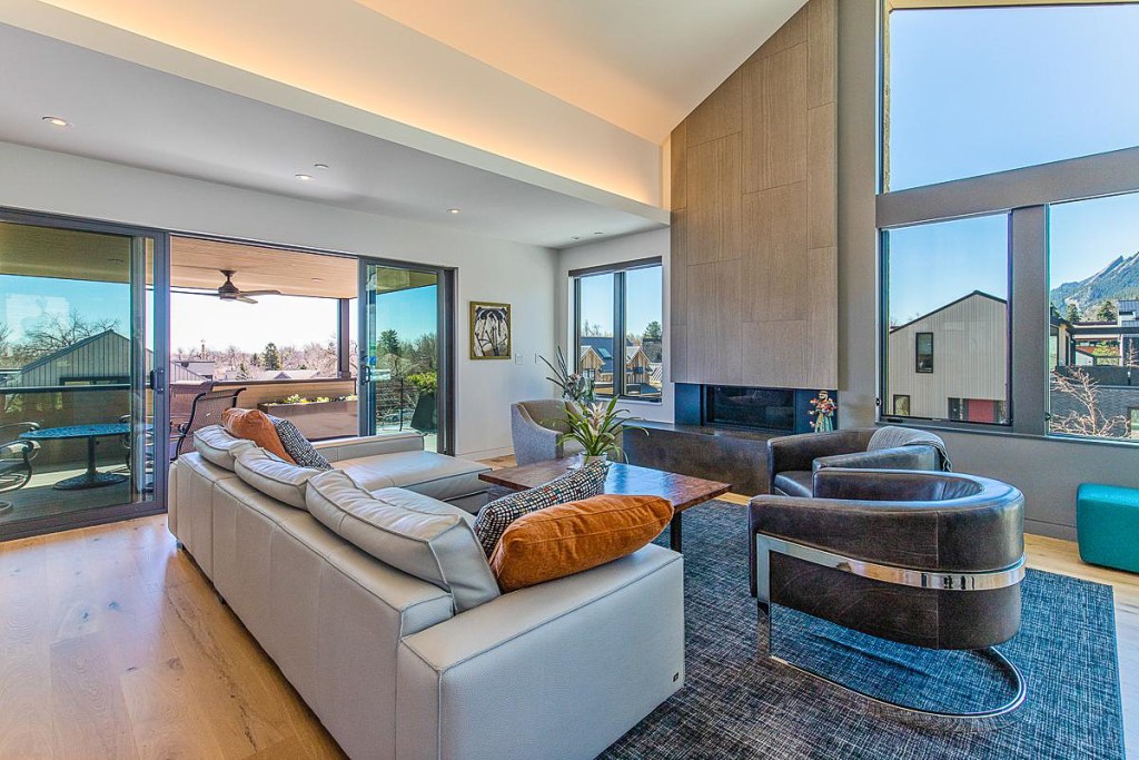 Modern living room with large windows and natural light, featuring a comfortable sofa, armchairs, and a coffee table, with a view of the outdoor landscape.
