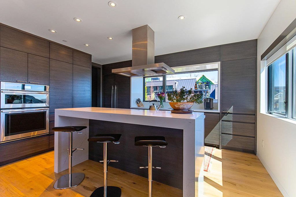 Modern kitchen featuring sleek cabinetry, a large island with bar stools, and ample natural light from surrounding windows.