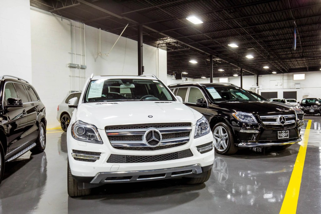 Display of luxury vehicles at a car dealership, featuring a white Mercedes-Benz SUV in the foreground and a black Mercedes-Benz SUV beside it inside a spacious showroom.
