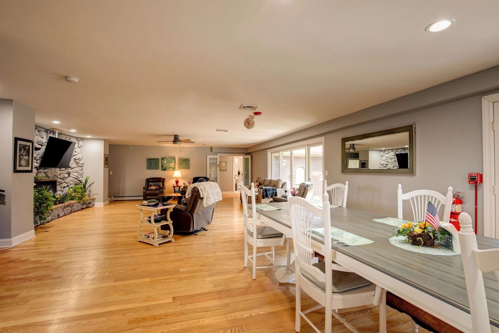 Spacious interior of a senior living community featuring a dining area with white chairs, a wooden table, and a cozy living room area with comfortable seating and natural light.