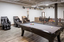 Interior view of a lounge area featuring a billiard table and massage chairs, with wooden flooring and a fenced-off play area.