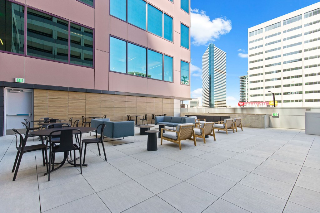 Outdoor terrace area with seating arrangements, featuring modern furniture and large windows of a commercial building in an urban setting.