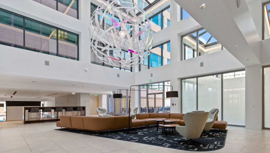 Modern commercial lobby featuring large windows, contemporary furniture, and a distinctive chandelier.