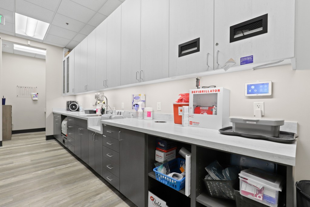 Interior view of a dental or medical facility featuring a countertop with various medical supplies, a defibrillator, and cabinets above.