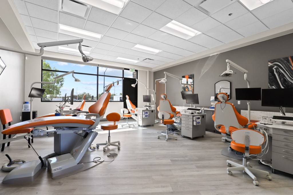 Interior view of a modern dental clinic featuring multiple dental chairs and equipment, with large windows allowing natural light.