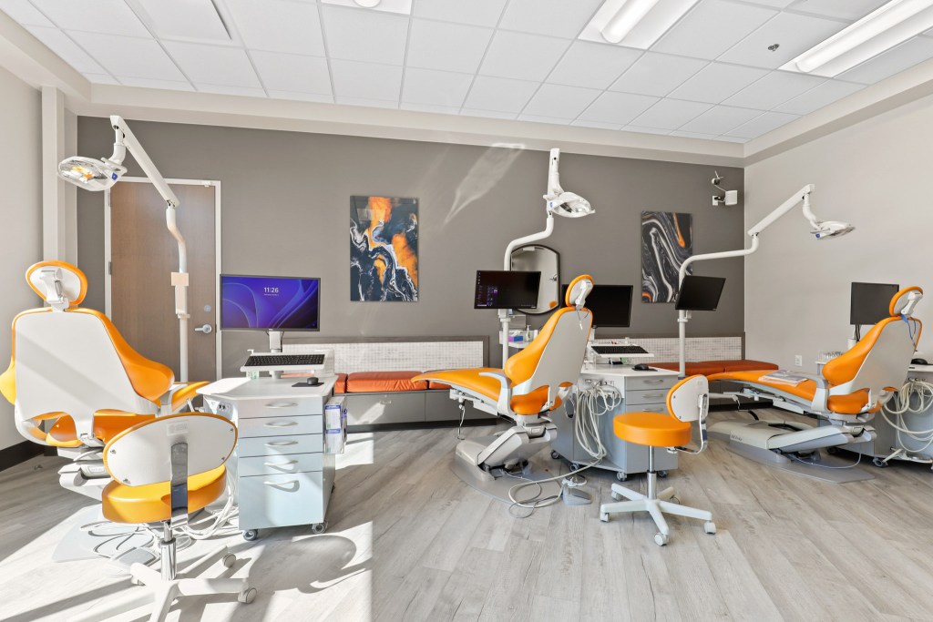 A modern dental clinic interior featuring dental chairs with orange accents, computers, and a sleek design.