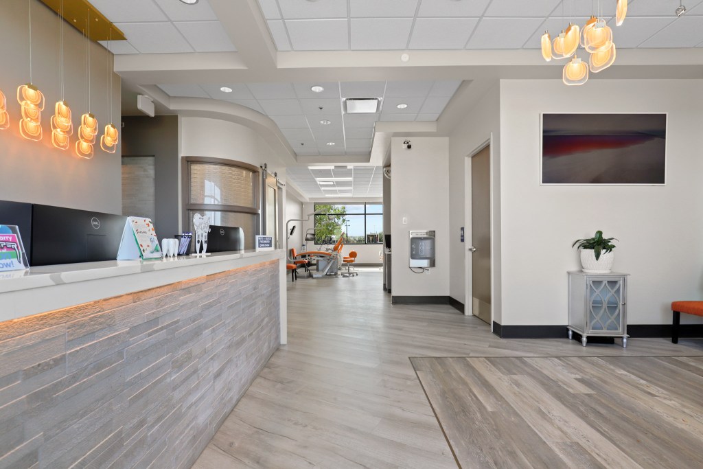 Interior of a modern dental clinic reception area with a stylish front desk, contemporary light fixtures, and waiting area furniture.