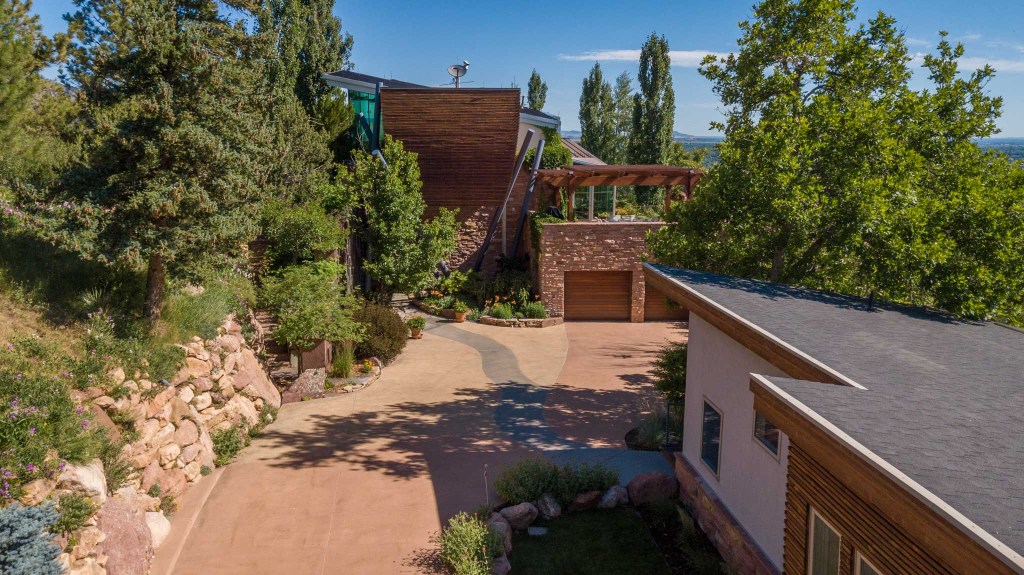 Aerial view of a modern home surrounded by greenery, showcasing a driveway, landscaped gardens, and a stone facade.