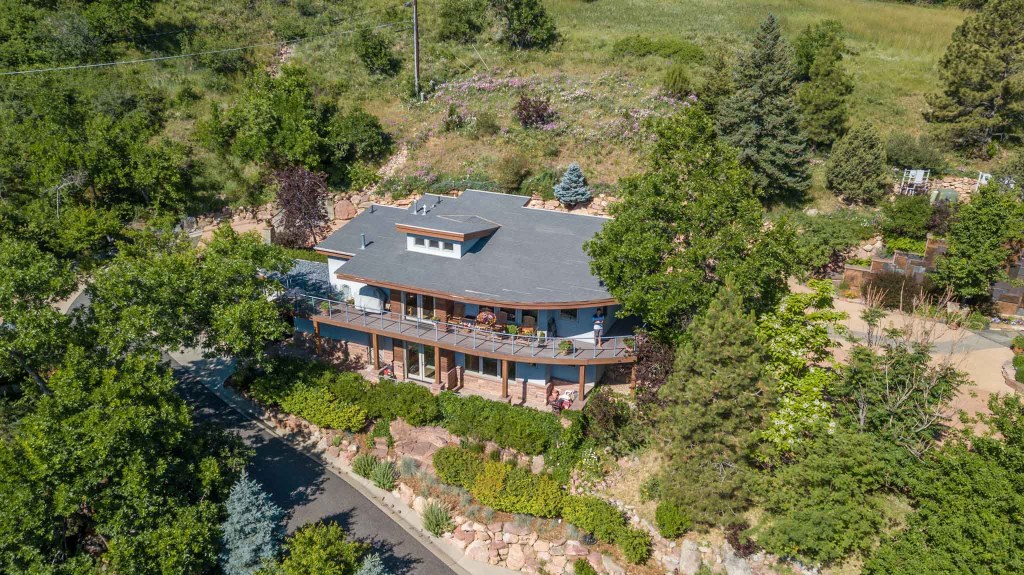Aerial view of a large residential home surrounded by lush greenery and landscaping, situated on a hillside.
