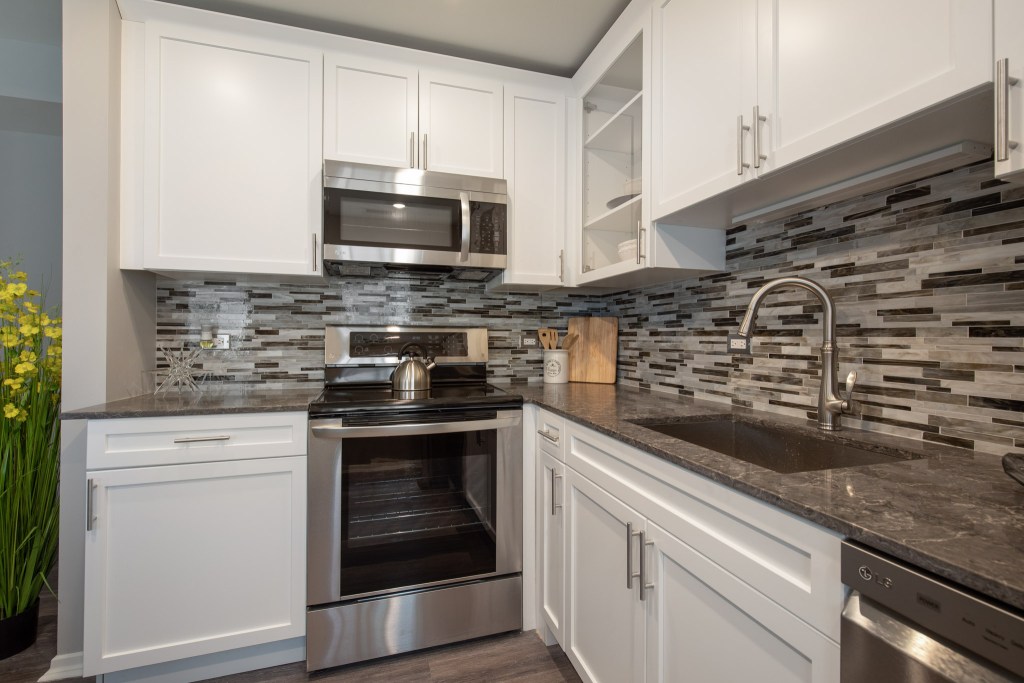 Modern kitchen with white cabinetry, stainless steel appliances, and a stylish backsplash featuring gray tones.