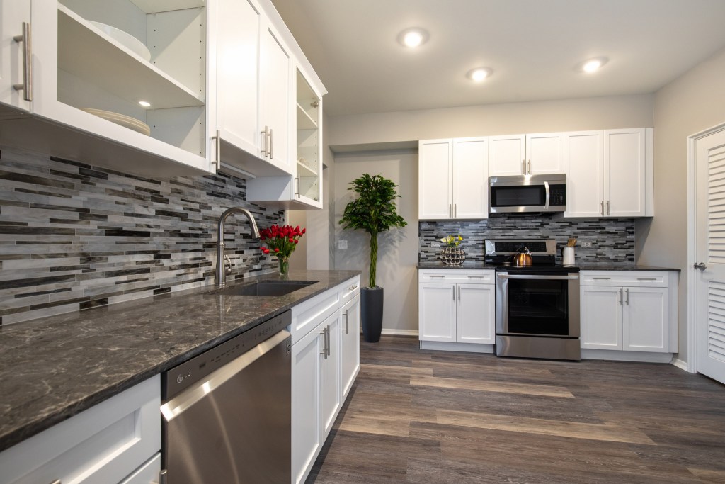 Modern kitchen featuring stainless steel appliances, white cabinetry, and a sleek dark countertop, with decorative flowers and greenery.