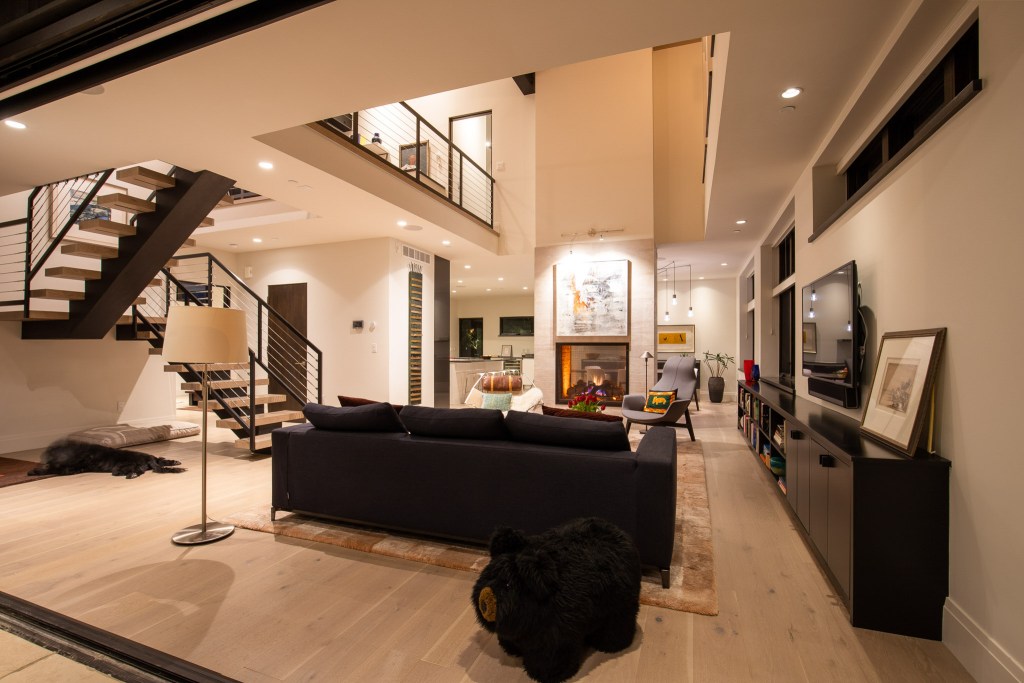Modern living room interior with a stylish staircase, dark sofa, and a cozy fireplace, featuring a contemporary design and warm lighting.