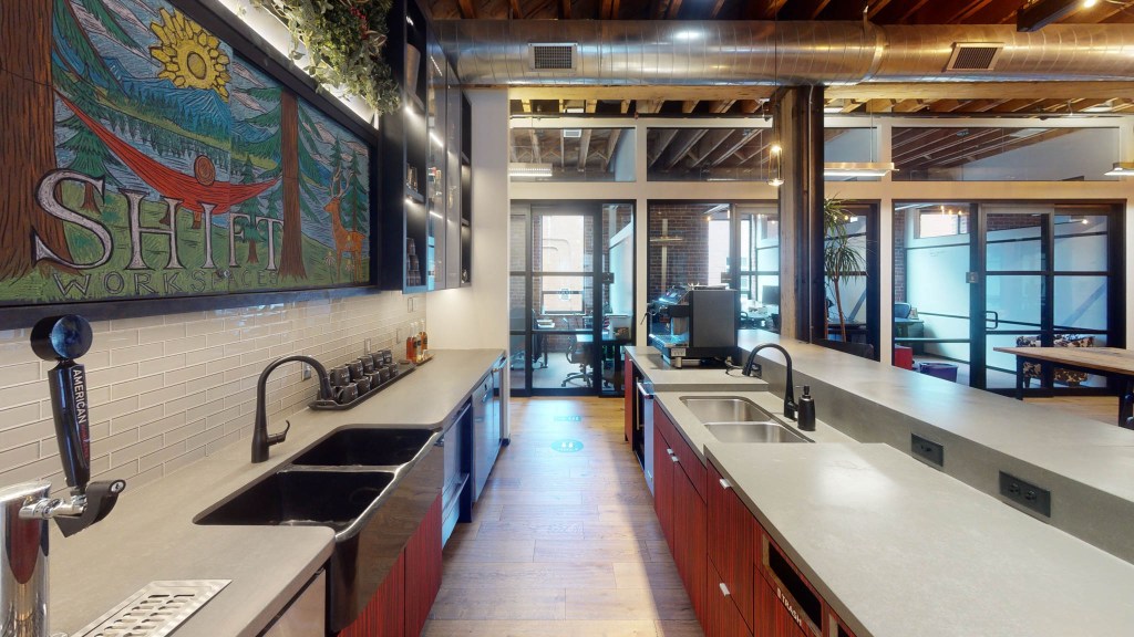 Interior view of a kitchen area in a co-working space featuring a colorful mural, modern appliances, and a sleek countertop.