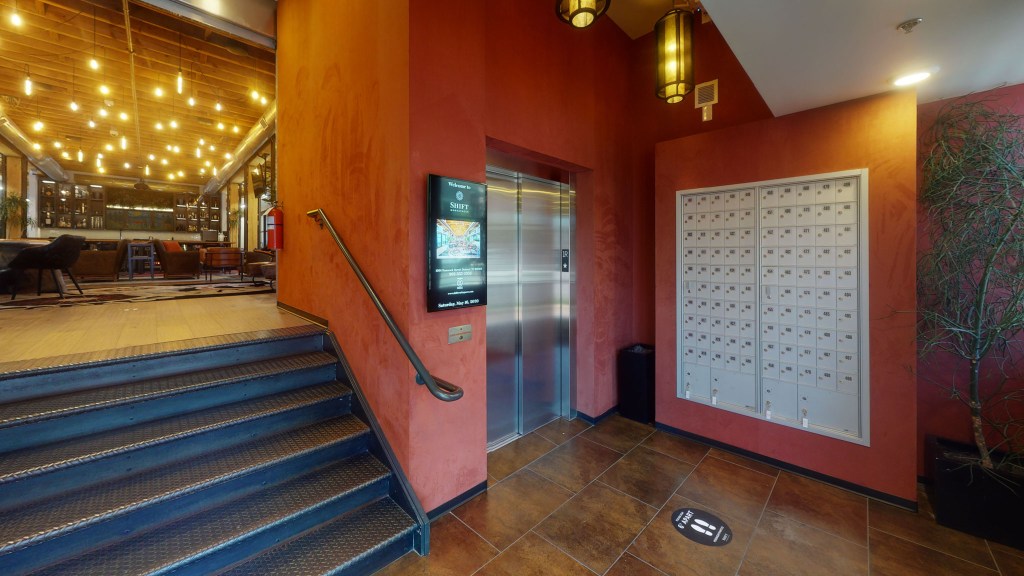 Interior entrance of a co-working space featuring an elevator, secured mailboxes, and warm lighting.