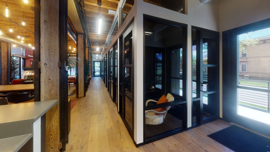 Interior view of a co-working space featuring a wooden floor, glass-walled meeting rooms, and a casual seating virtual tour by West 360 digital.