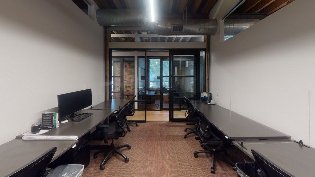 Co-working space interior featuring multiple workstations with computer screens and a glass door leading to another room.