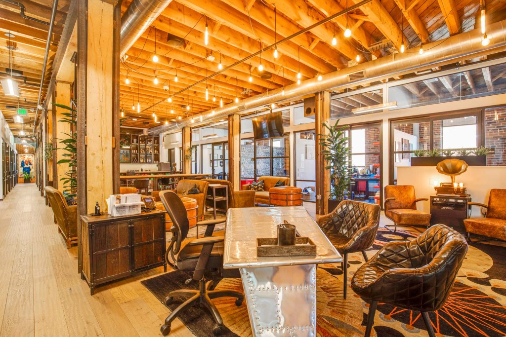 Interior view of a co-working space featuring a blend of modern and rustic design with large windows, wooden beams, and stylish seating areas.