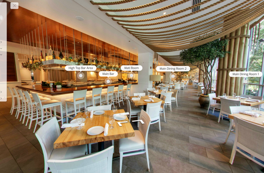 Spacious interior of Avli on the Park restaurant showcasing contemporary Mediterranean design with large windows letting in natural light, wooden tables set for dining, plush seating, and decorative pendant lighting creating a warm and inviting atmosphere.