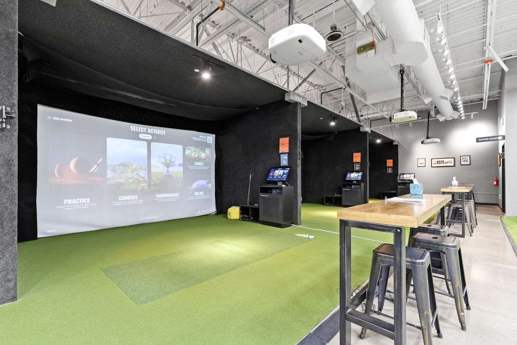 Interior view of The Swing Bays golf simulator facility featuring practice areas and interactive screens.