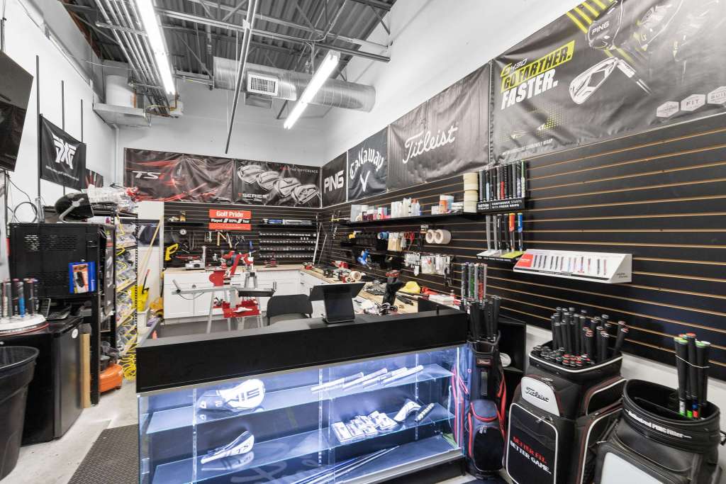 Interior view of a golf shop showcasing various golf equipment, tools, and accessories on display. The walls are adorned with branding and logos from leading golf brands, and there are workstations for club fitting and repairs.