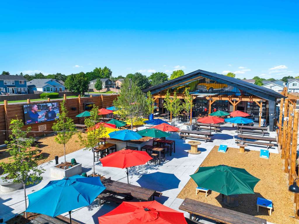 Aerial view of Billy Birch Pub and Yard showcasing colorful patio umbrellas, outdoor seating areas, and the pub's rustic structure against a clear blue sky.