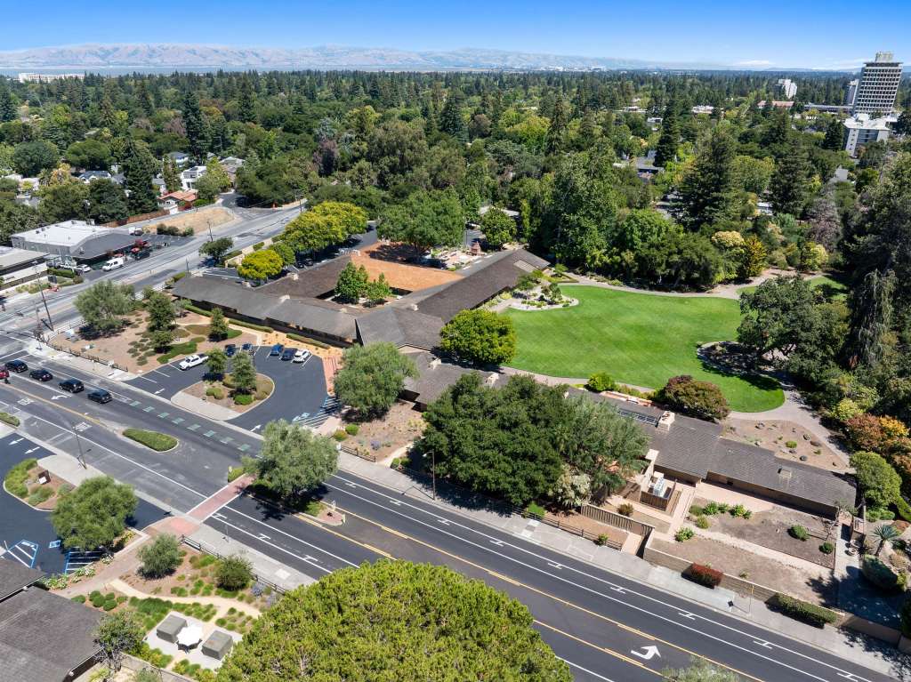 Aerial view of Willow Workplace in Menlo Park, showcasing co-working spaces surrounded by greenery and trees, with roads and parking areas visible.