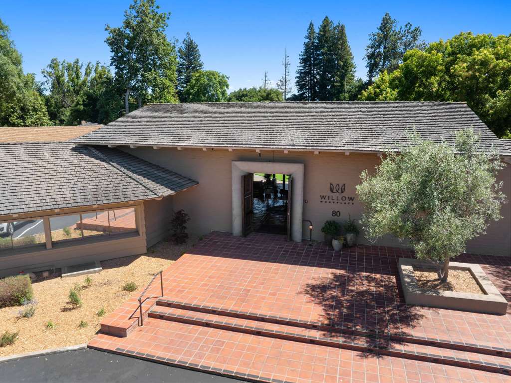 Aerial view of the entrance to Willow Workplace in Menlo Park, showcasing a modern building with a welcoming entrance and lush greenery surrounding it.