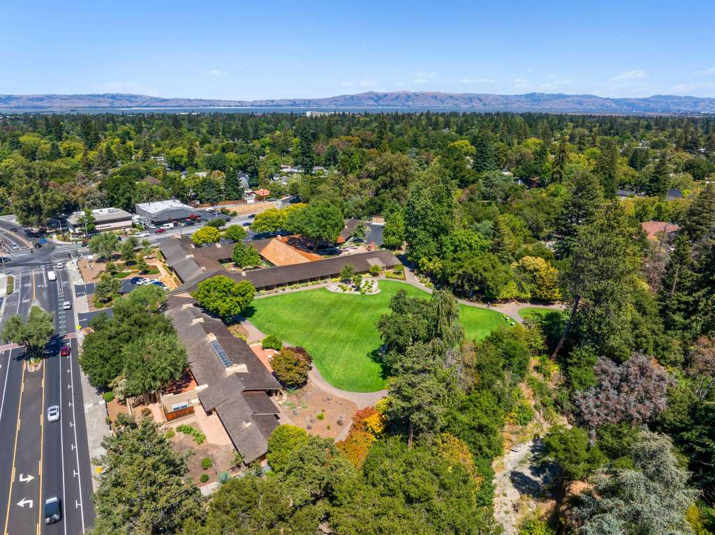 Aerial view of Willow Workplace in Menlo Park, showcasing lush greenery, spacious outdoor areas, and modern buildings amidst a scenic landscape.