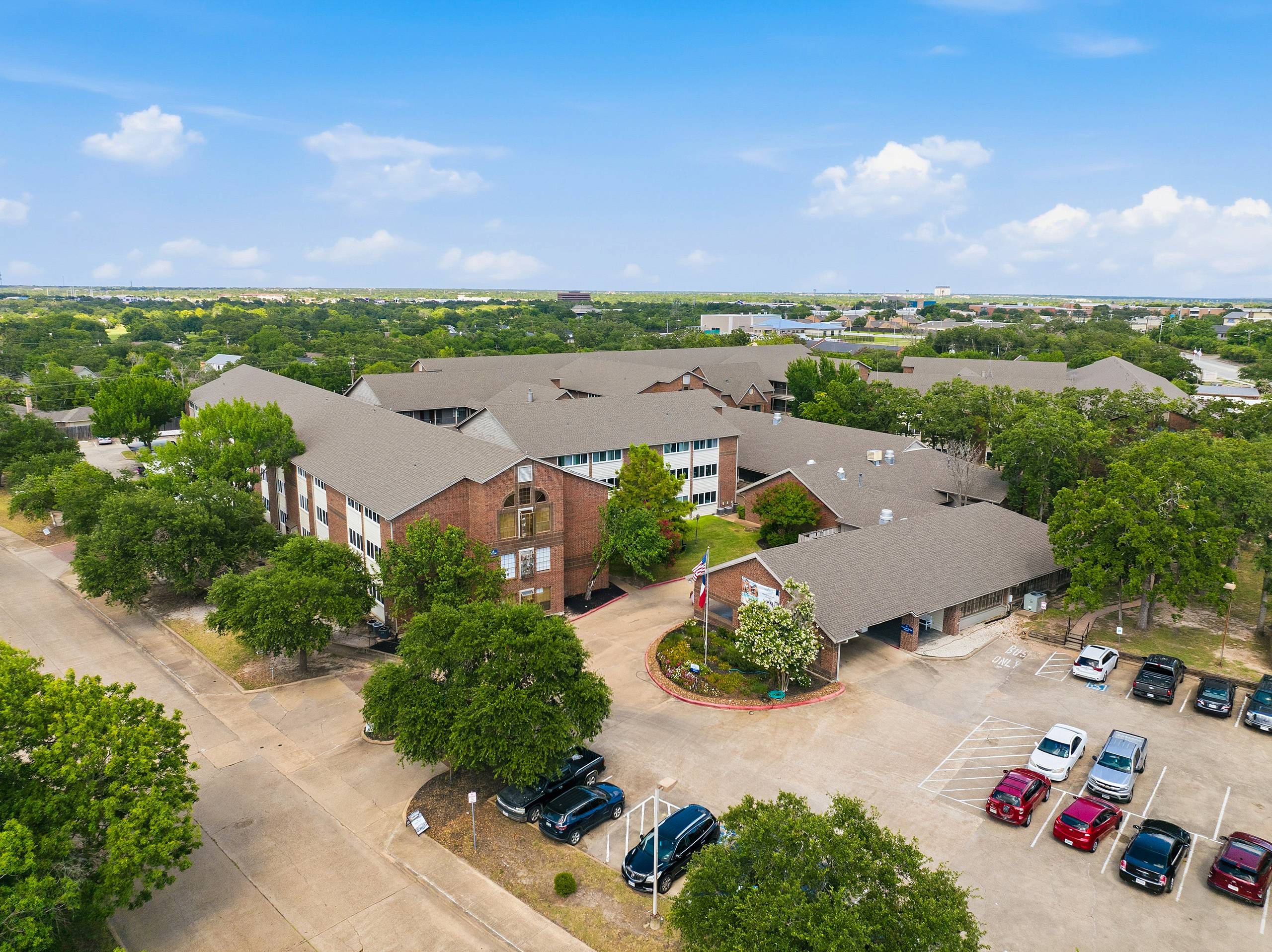 Drone view of the entrance, clubhouse and three-story brick buildings at Serenity at Briarcrest in Bryan, Texas