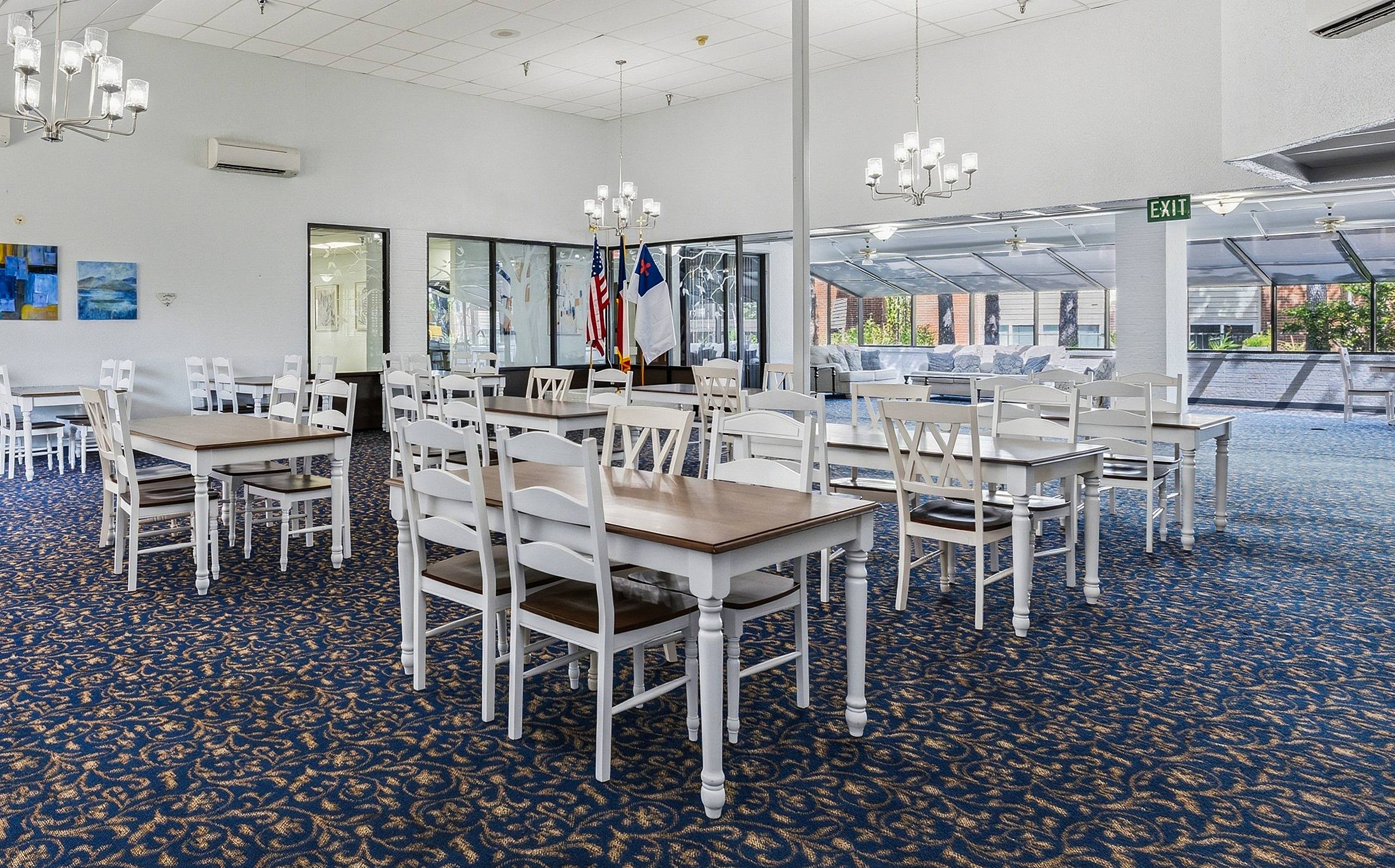 Chandelier-lit community dining room with white tables at Serenity at Briarcrest in Bryan, Texas