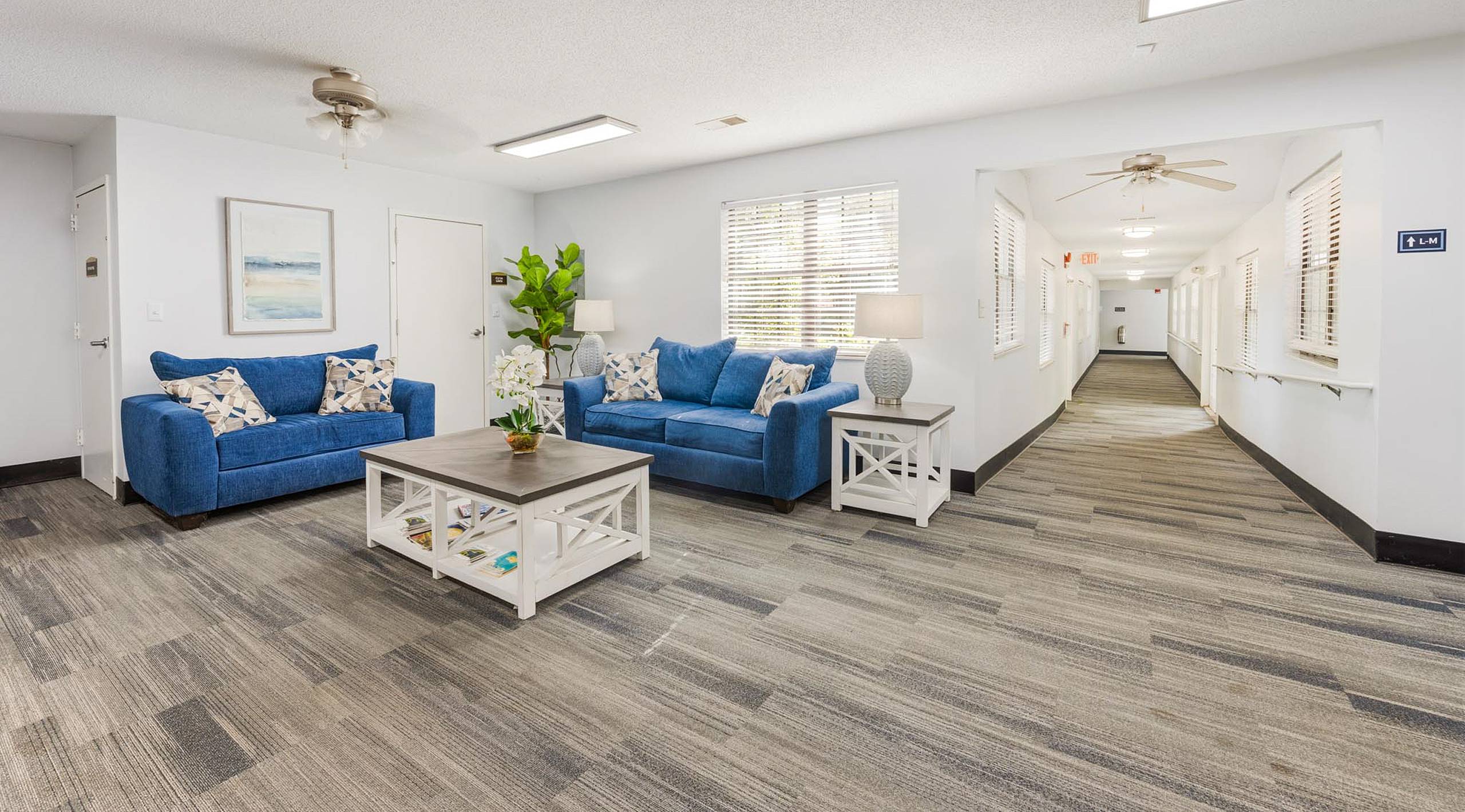 Resident lounge with blue loveseats and handrail hallway at Serenity at Easley 55+ apartments